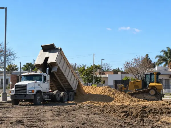 Camión volcador volcando material frente a una casa